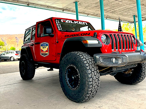 Bright cherry red elevated Jeep Wrangler Rubicon parked under an awning with a desert in the background