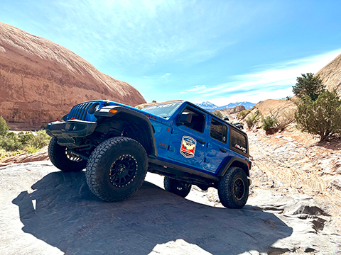 Blue JLU Jeep Wrangler Rubicon climbing a large rock